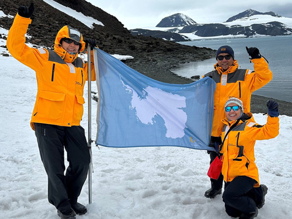 three people in artic setting, holding a flag