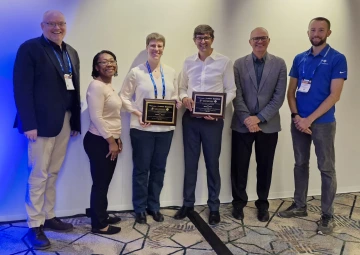 group of six people standing, two are holding awards