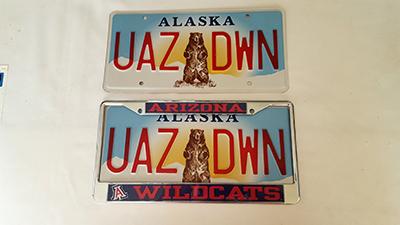 Two Alaska license plates, with "UAZ" on one side of a bear illustration and "DWN" on the other