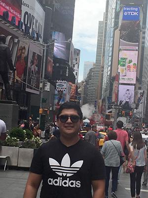 A man in black sunglasses and a black shirt standing in the middle of Times Square