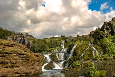 A man stands overlooking gentle waterfalls cascading down a mountainside