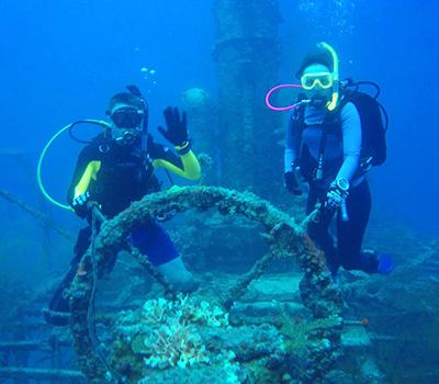 A pair of scuba divers waving in front a sea wreck
