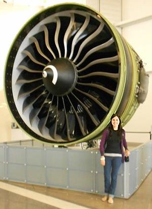 A woman stands in front of an enormous turbine at least twice as tall as she is