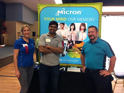 Two men and a woman standing in front of a poster that says "Micron: Your Mind. Our Memory."