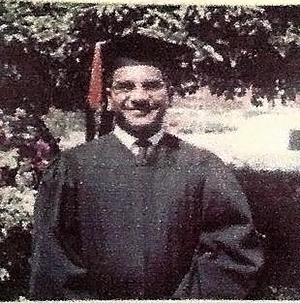 A man wearing a cap and gown standing before some bushes