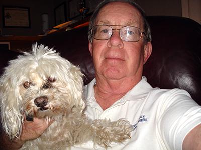 A man with wire-rimmed glasses holds a fluffy white dog