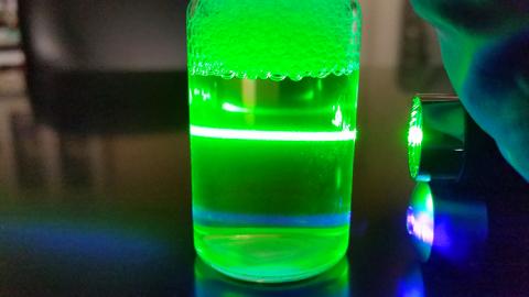 A green laser illuminates a beaker full of clear liquid
