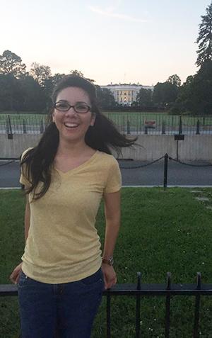 A woman with long hair wearing a yellow shirt stands in front of the White House in Washington, D.C.