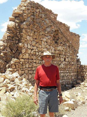 Paul Smith, wearing a red shirt and floppy hat, stands in front of a crumbling stone wall about twice his height