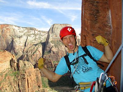 A man in climbing gear climbing a mountain makes a funny, celebratory face