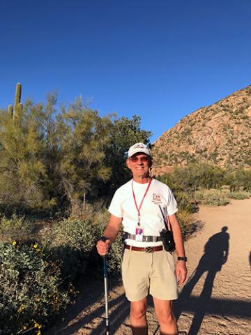A man standing in the desert and holding a hiking pole while smiling at the camera