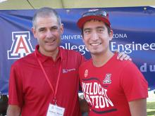 Two men in red University of Arizona T-shirts stand in front of a blue College of Engineering banner