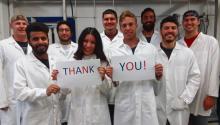 A group of men and women in lab coats standing in a group, two people in front holding a sign that reads "thank you"