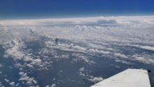A photo from the viewpoint of a plane, looking down at clouds and the ocean