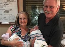 An older couple hold two newborn babies in a hospital room.