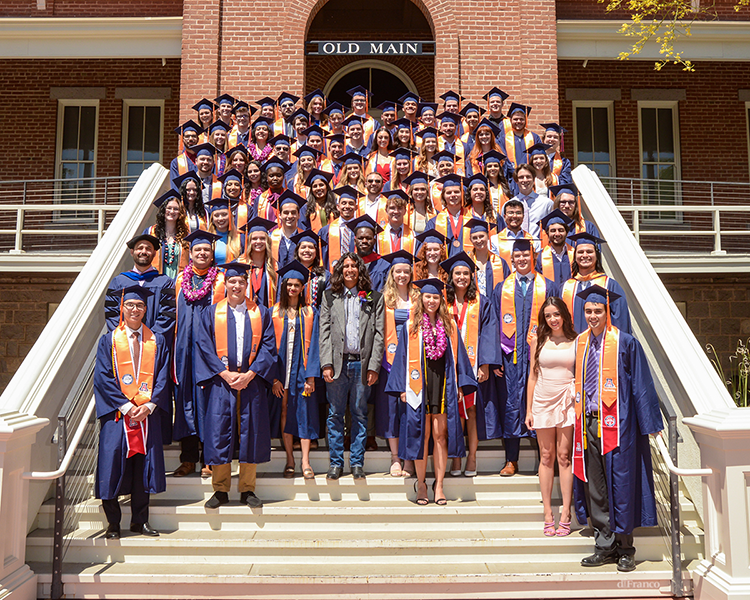 students in regalia, standing on the steps of UArizona Old Main