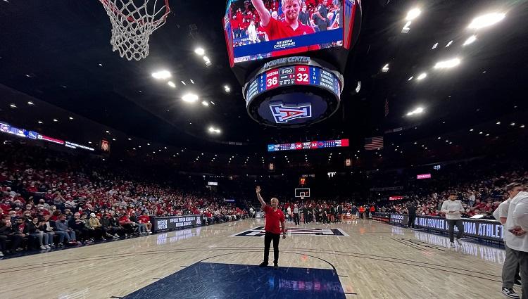 Byron Hempel in middle of the University of Arizona basketball court, with his image on a large screen behind him.