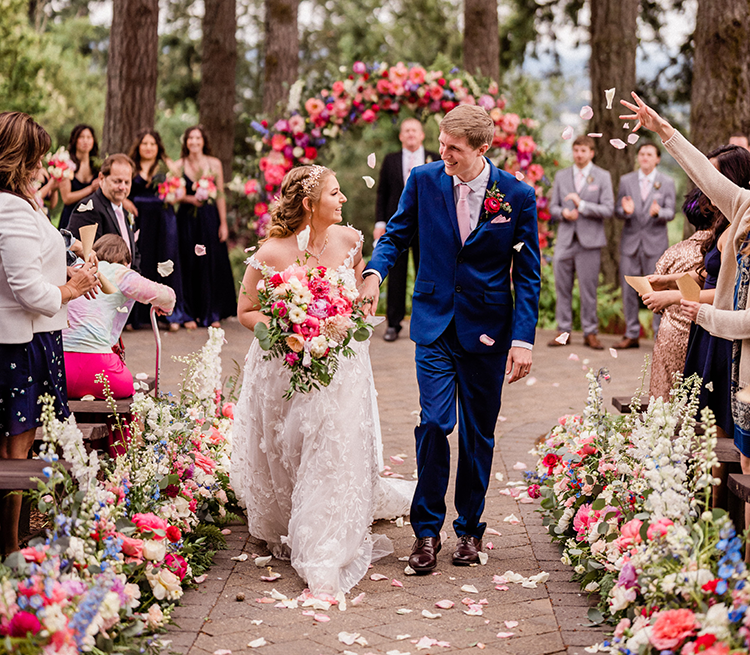 bride and groom under floral archway, surrounded by people