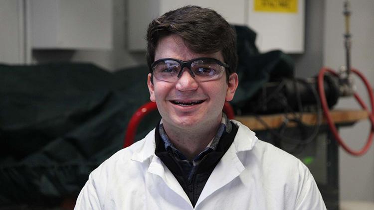 Gabriel Schirn smiling, wearing protective eyewear and a lab coat in a chemical engineering lab