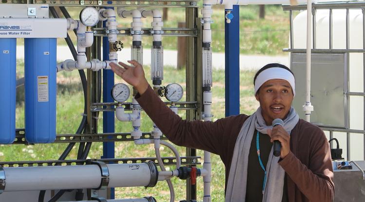 Diné College student and Indige-FEWSS participant Larry Moore demonstrates the solar-powered water filtration system to community members on Navajo Nation.