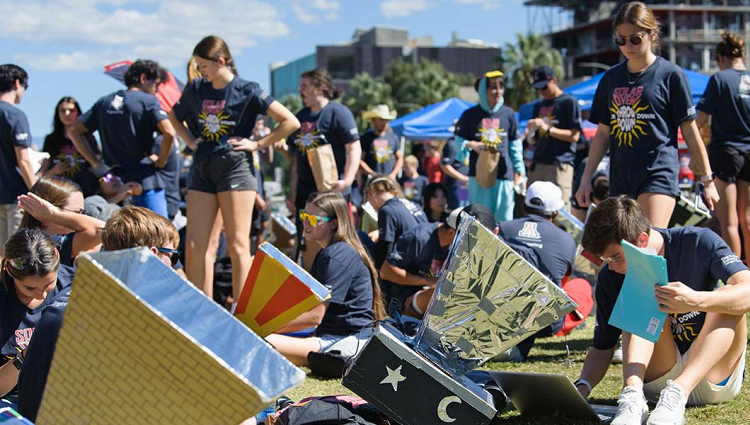 A crowd of students working on their solar ovens in an open field