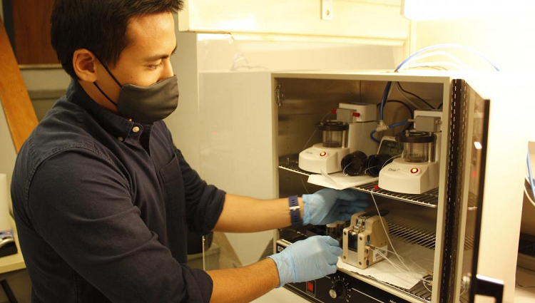 Suchol Savagatrup, wearing gloves and a mask, reaching into a cabinet in his laboratory.