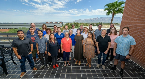 group of people standing on rooftop patio, palm tree in background