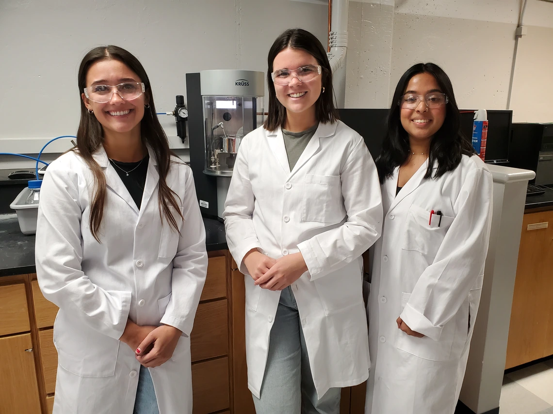 Three people wearing white lab coats, smiling