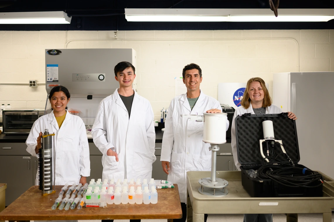 Four people in white lab coats stand behind a desk.