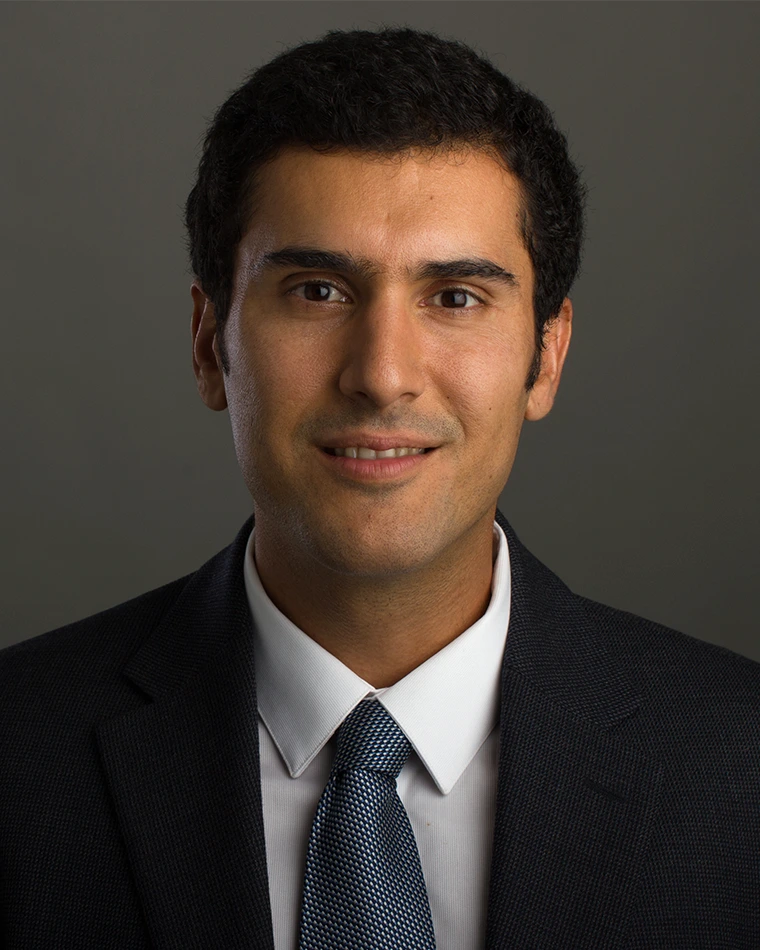 headshot of person wearing dark suit, blue tie and white shirt