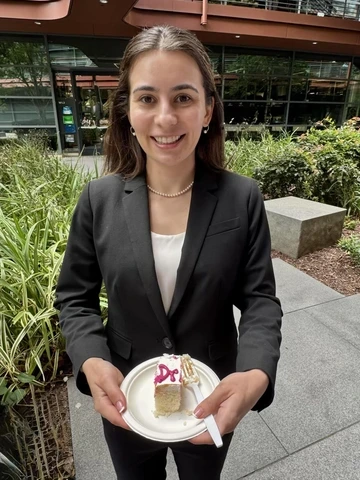 person with long dark hair, wearing gray business suit, holding a piece of cake