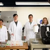 Four people in white lab coats stand behind a desk.