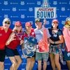A group of people in red shirts stand in front of a blue background.